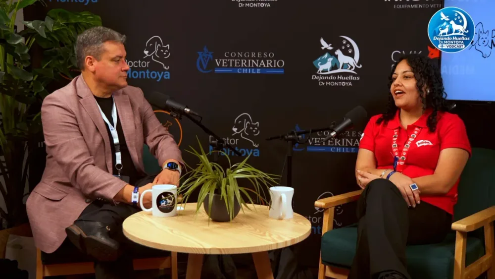Un hombre y una mujer con polera roja de Holliday conversan sentados en un estudio con micrófonos y una mesa de madera; detrás, los logos del Congreso Veterinario y de Dejando Huellas.